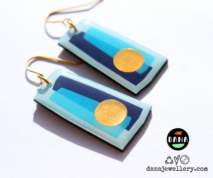 A pair of colourful drop earrings handmade in Ireland featuring abstract geometric patterns in blue shades with a gold circle detail, made from recycled vinyl records, with gold-plated hypoallergenic hooks.