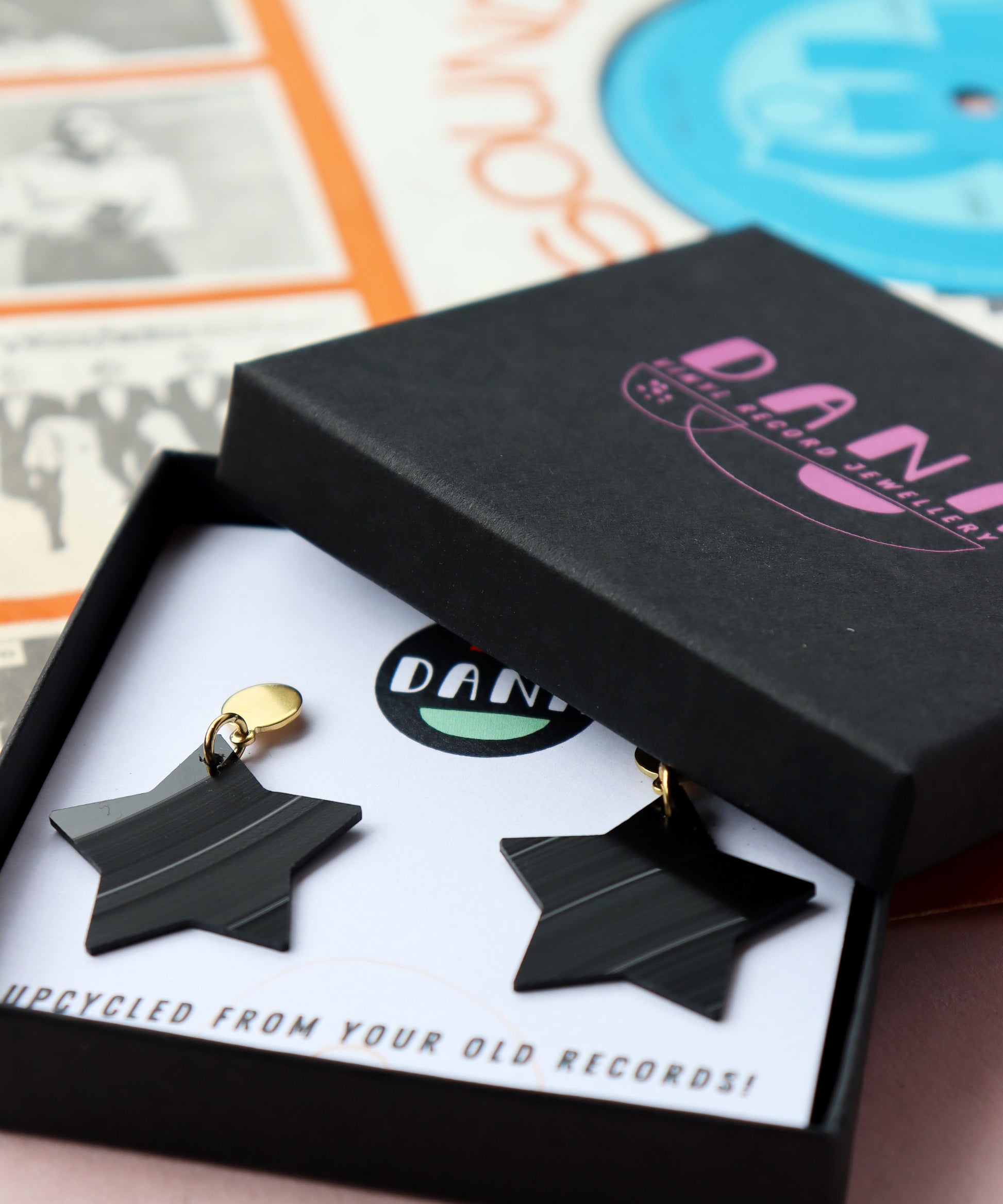 Black star earrings with gold posts handmade in Ireland from recycled vinyl record displayed in a branded DANA Jewellery box.