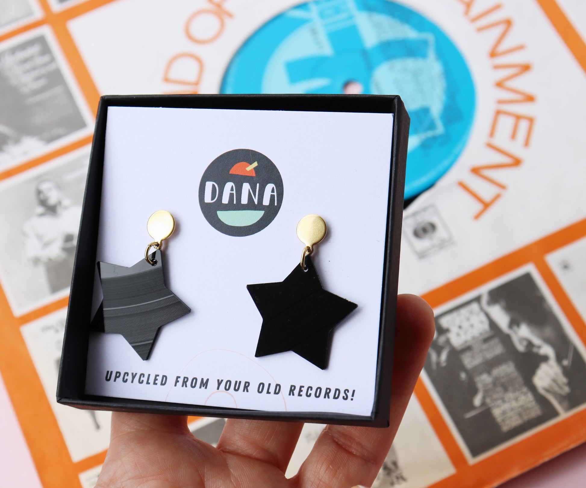 Black star earrings with gold posts handmade in Ireland from recycled vinyl record displayed in a branded DANA Jewellery box.