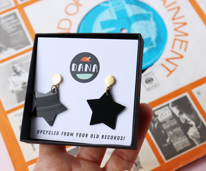 Black star earrings with gold posts handmade in Ireland from recycled vinyl record displayed in a branded DANA Jewellery box.
