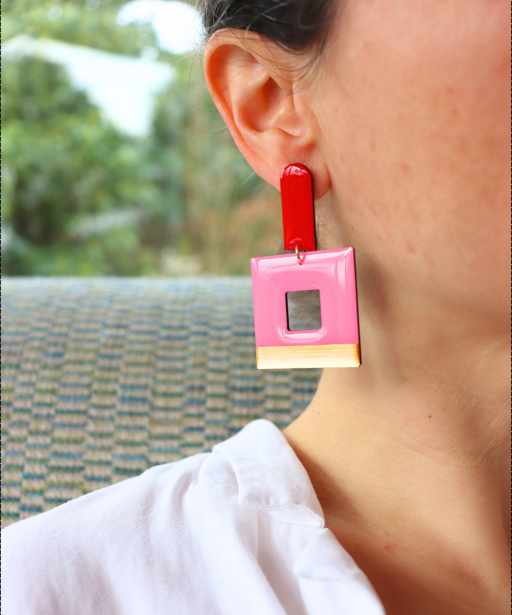 A statement geometric earring displayed on model with bright red long arch post an dangly square contour in pink with a shiny gold band running along the base. Handmade in Ireland from recycled vinyl record by DANA Jewellery.