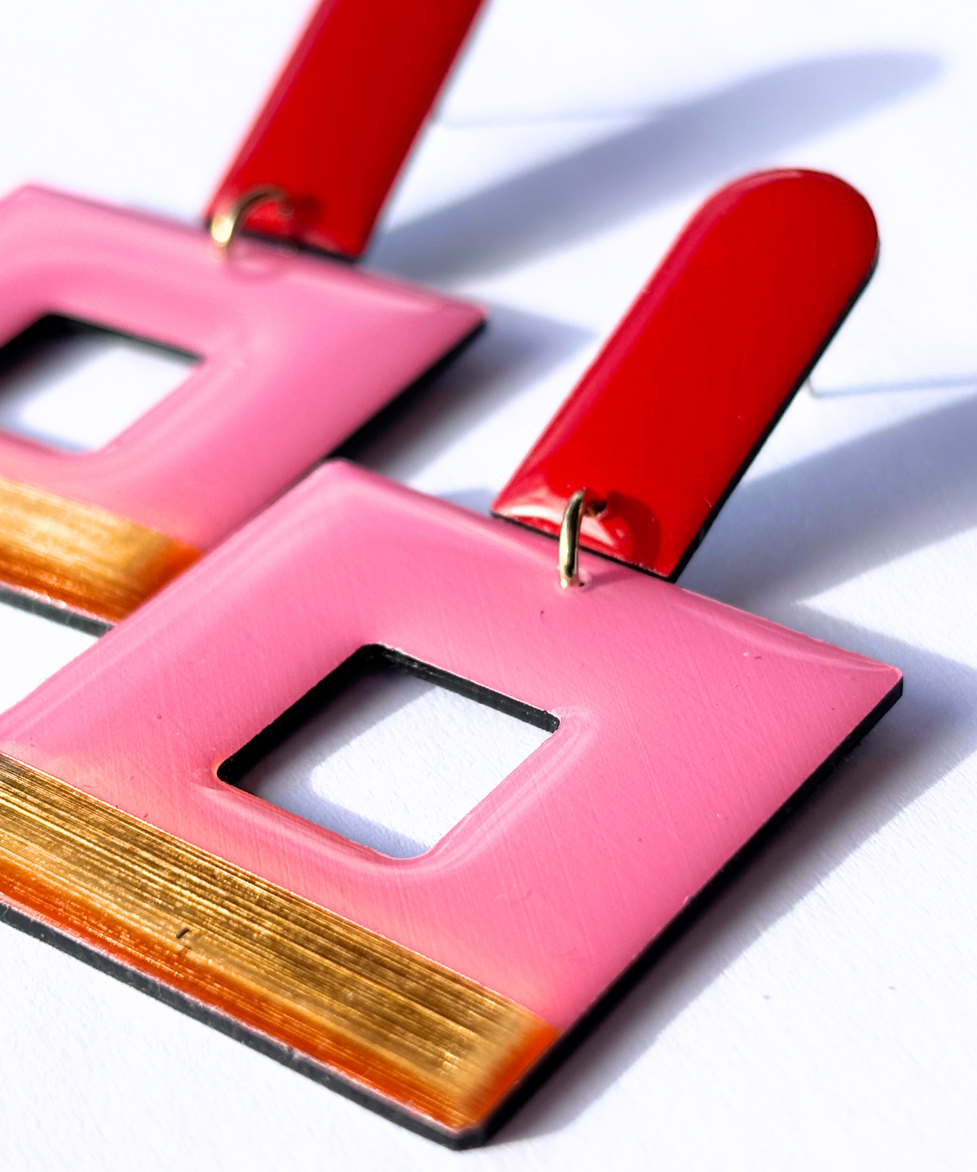 A pair of eco friendly geometric statement earrings with red long arch posts, pink, and gold colours with a bold design, crafted in Ireland from recycled vinyl record. 