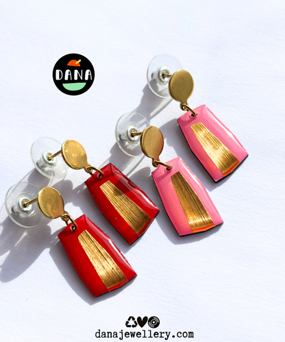Modern minimalist earrings handmade in Ireland in pink, red and gold attached to gold-colored posts, displayed on a clear surface with the brand name 'dana' and the website 'dananajewellery.com'.