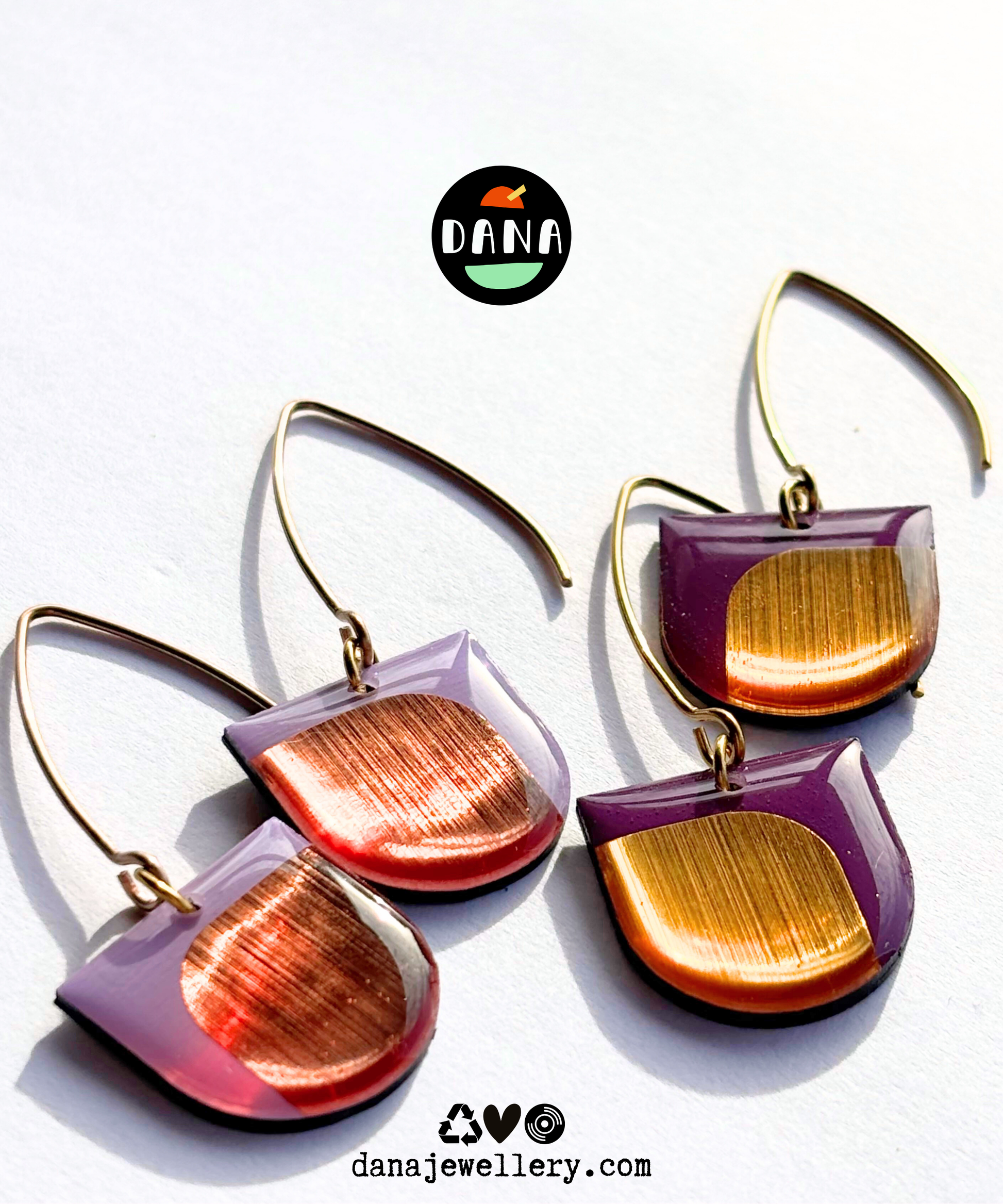 Pair of colourful earrings handmade in Ireland with purple and gold design on a white background, featuring the DANA brand.